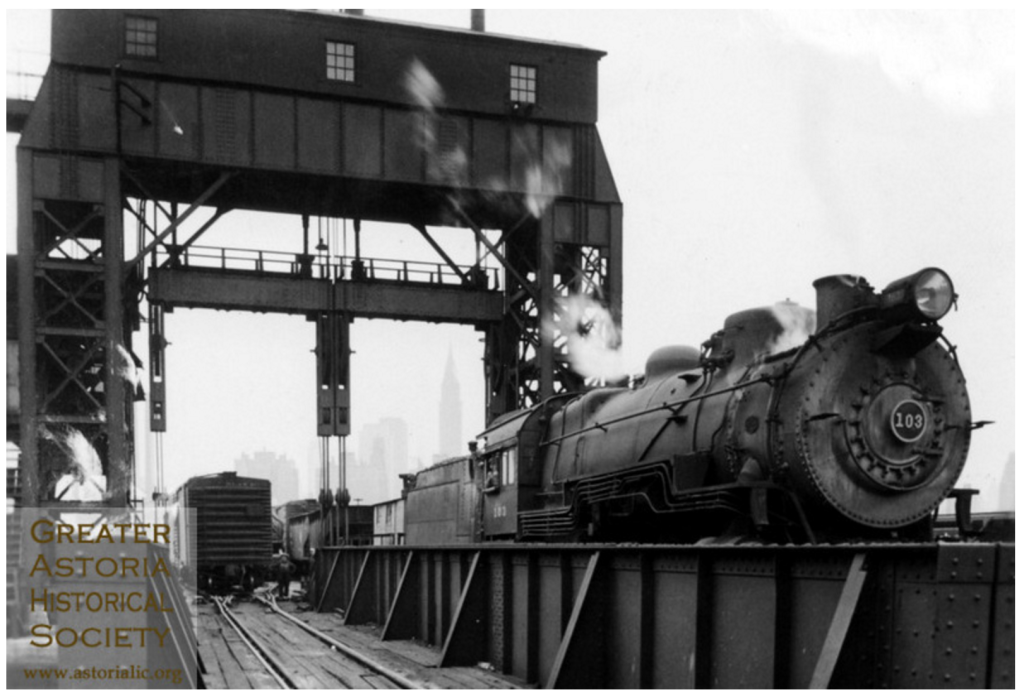 En bild från när förra seklet var ungt. Tågpromen lyfts till rätt nivå av kranen över spåren. Foto: Greater Astoria Historical Society